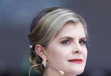 Costa Rica’s New President Publicly Entrusts Her Government to the Virgin of the Angels Portrait of a woman at a formal event wearing a red, white, and blue sash and a headset microphone, looking to the side.