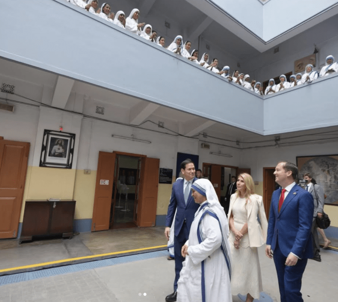 Screenshot 2026-05-26 at 6.53.25 PM Nuns in white habits stand along an upper-level balcony as formally dressed visitors walk through a pale hallway.