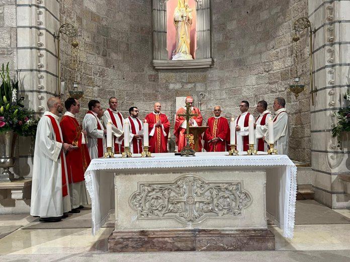 Catholic Mass scene with priests in red and white vestments around a decorated altar, candles lit, in a stone chapel.