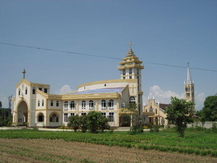 Large ornate church with white and gold exterior, arched windows, and a tall bell tower under a clear blue sky.