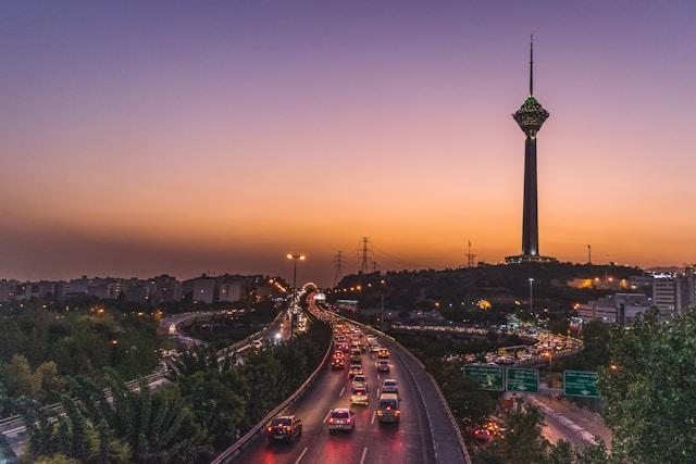 mohammad-amirahmadi-ShZzflXymPI-unsplash Evening cityscape with a busy highway and a tall illuminated tower on a hill at sunset.