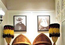 Hawaii Marks 200 Years of Catholic Missionary Legacy with Jubilee Year Celebration Two wooden arched display cases containing coffins and ceremonial items, flanked by tall feathered torches, with portraits on the wall behind.