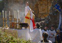 Holy Mass Returns to Bayham Abbey After Five Centuries, Marking Premonstratensian Milestone A priest lifts his hands in blessing at an outdoor altar with tall candle holders during a religious ceremony.