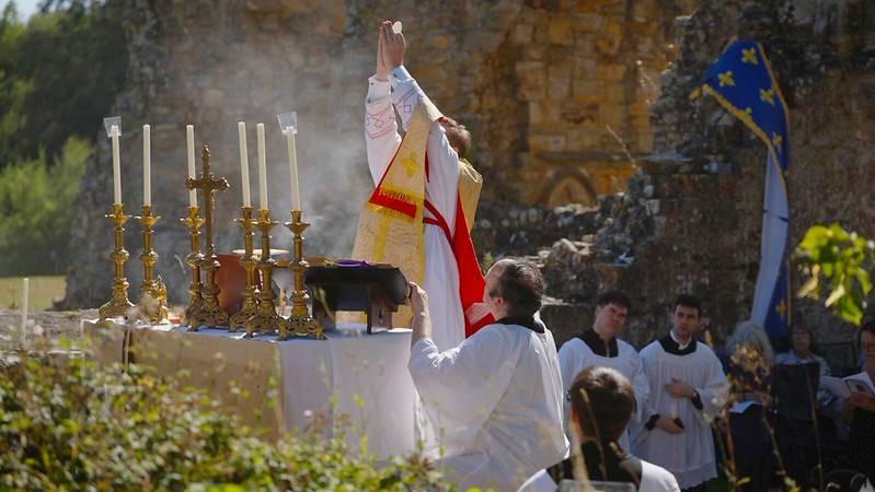 Holy Mass Returns to Bayham Abbey After Five Centuries, Marking Premonstratensian Milestone A priest lifts his hands in blessing at an outdoor altar with tall candle holders during a religious ceremony.