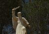 Fatima and Our Lady of Mount Carmel: from Carmel to the Kingdom of Mary Stone statue of a bearded robed man holding a curved blade aloft, standing on a pedestal with multilingual inscriptions, in a wooded park setting.