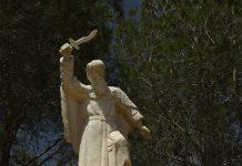 Fatima and Our Lady of Mount Carmel: from Carmel to the Kingdom of Mary Stone statue of a bearded robed man holding a curved blade aloft, standing on a pedestal with multilingual inscriptions, in a wooded park setting.
